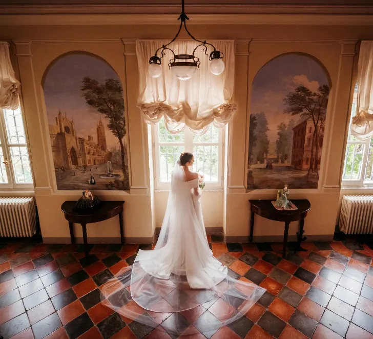 la-sposa-si-avvicina-alla-finestra-vista-di-un-corridoio-minuziosamente-affrescato-con-mobilio-del-700-e-pavimentazione-rossa-e-nera-del-tempo